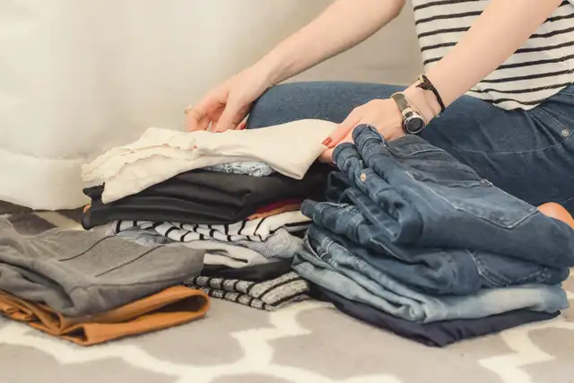 Hands sorting folded denim and tops into piles